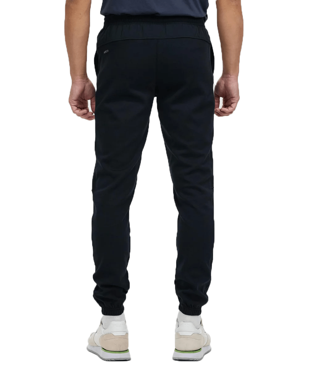 Man wearing black Canterbury Tempo Vapodri Hybrid Cuffed Pant and white sneakers, viewed from behind, standing against a plain white background.
