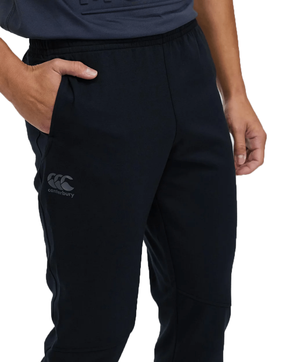 Close-up of a person wearing dark Canterbury Tempo Vapodri Hybrid Cuffed Pants with the logo on the left thigh, focusing on the waistband and upper leg.
