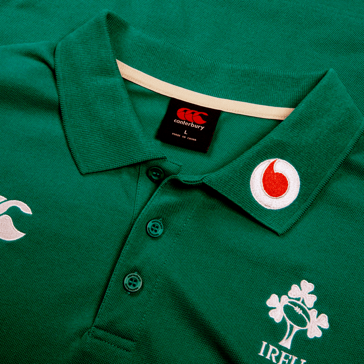 The Ireland 25/26 Team Polo by Canterbury is a green cotton shirt featuring embroidered Canterbury and Vodafone logos plus a shamrock crest; includes buttons and is perfect for training.