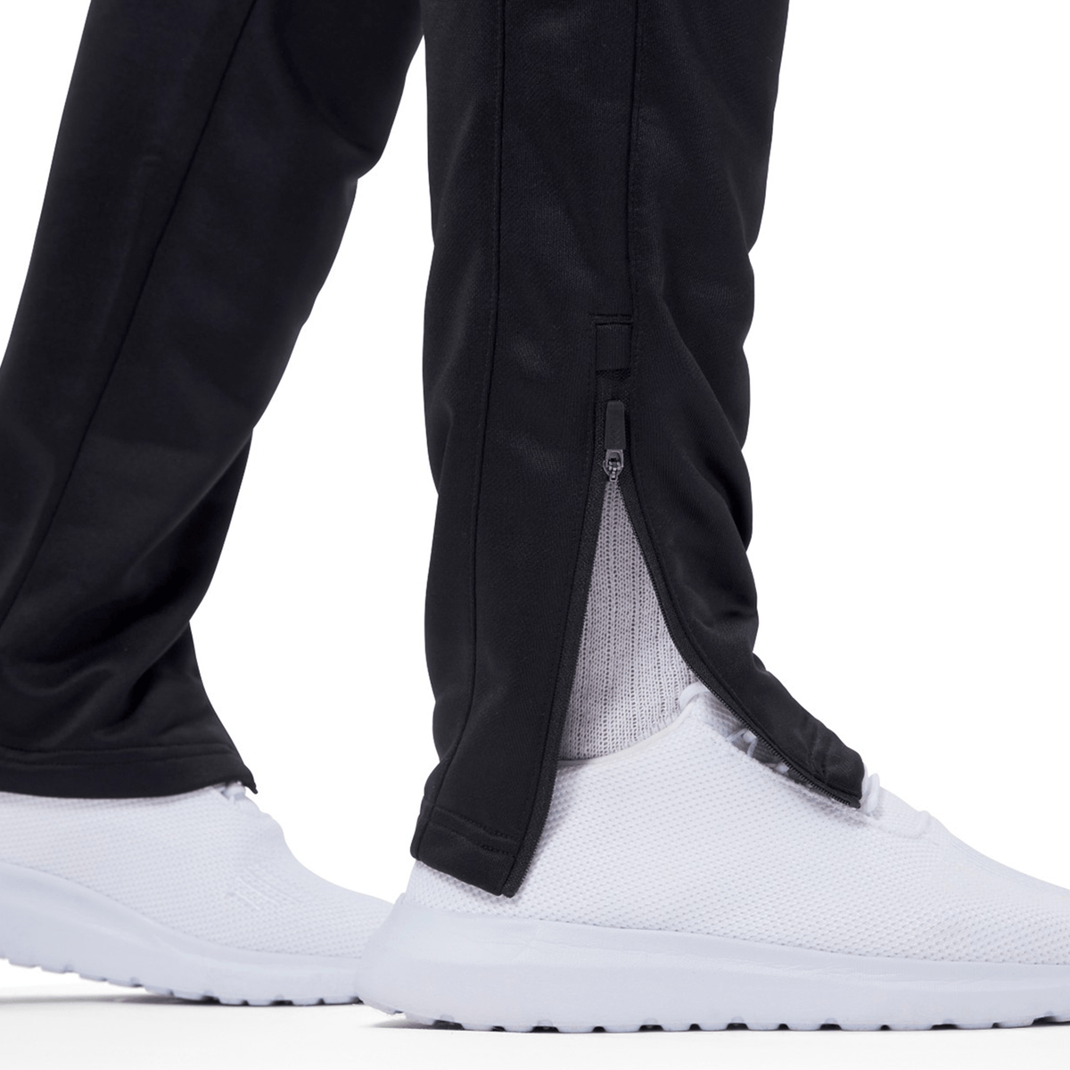 Close-up of an Irish rugby fan wearing Ireland 24 Poly Knit Pant by Canterbury with a zipper at the ankle and white lightweight athletic shoes. The pants are slightly open at the zipper, revealing white socks.