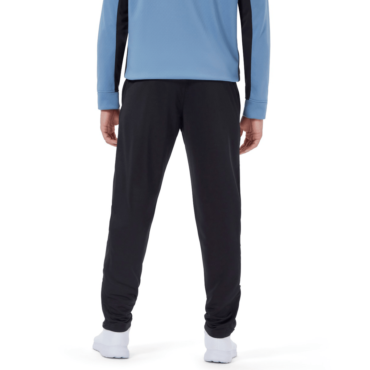 A person stands facing away, wearing a blue long-sleeve top, black Ireland 24 Poly Knit Pant by Canterbury, and white sneakers.