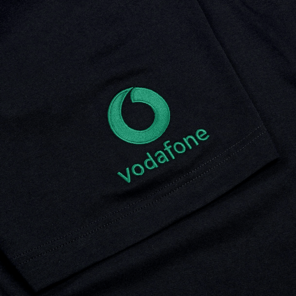 A close-up of a black cotton T-shirt with a green Vodafone logo and text embroidered on it, resembling the style of the Ireland Team Cotton T-Shirt 24 by Canterbury.