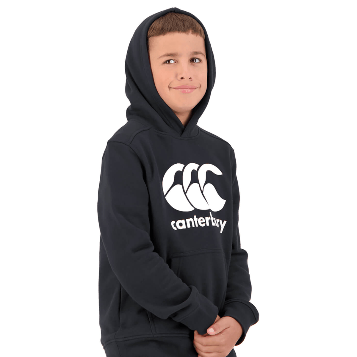 A young boy in a black Canterbury Anchor Hoodie with a white logo stands facing the camera, hands clasped in front. The fleece-lined hoodie adds an extra layer of comfort to his casual yet stylish look.