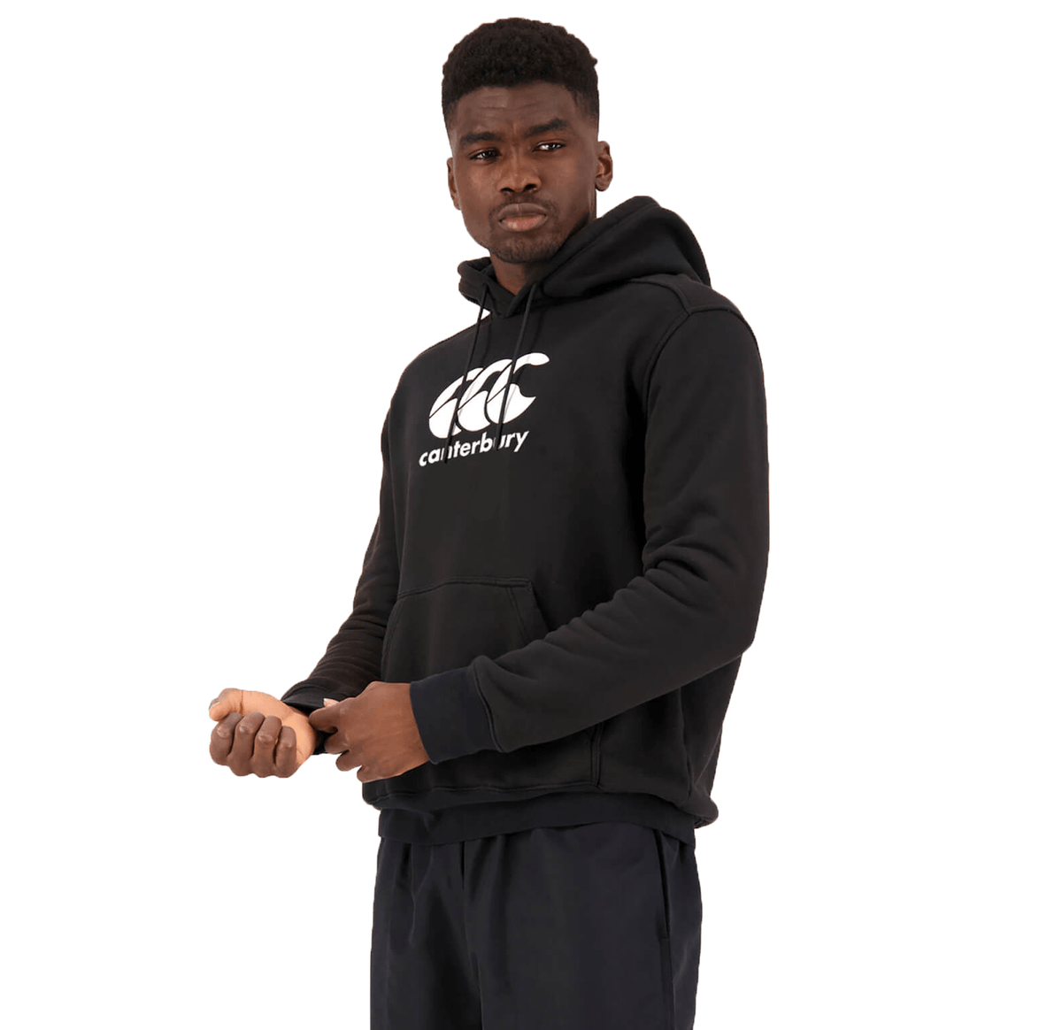 A person wearing the Canterbury Anchor Hoodie, a black fleece-lined hoodie featuring white text and the Canterbury logo, stands against a white background. They have a thoughtful expression while looking to the side and adjusting their sleeve.