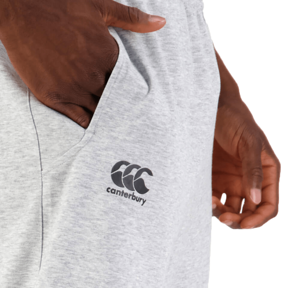 Close-up of a person's hand touching the fabric of a gray Canterbury Tempo Vapodri Hybrid Cuffed Pant.