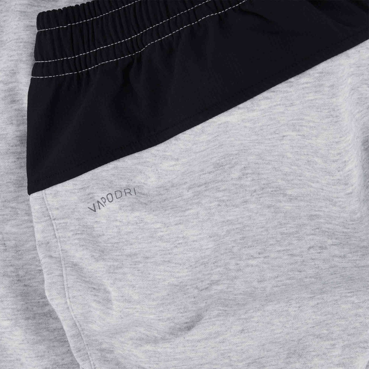 Close-up of Canterbury Tempo Vapodri Hybrid Cuffed Pant in gray and black features an elasticated waistband, with “Vapodri” subtly printed on the gray fabric to highlight its sporty design.