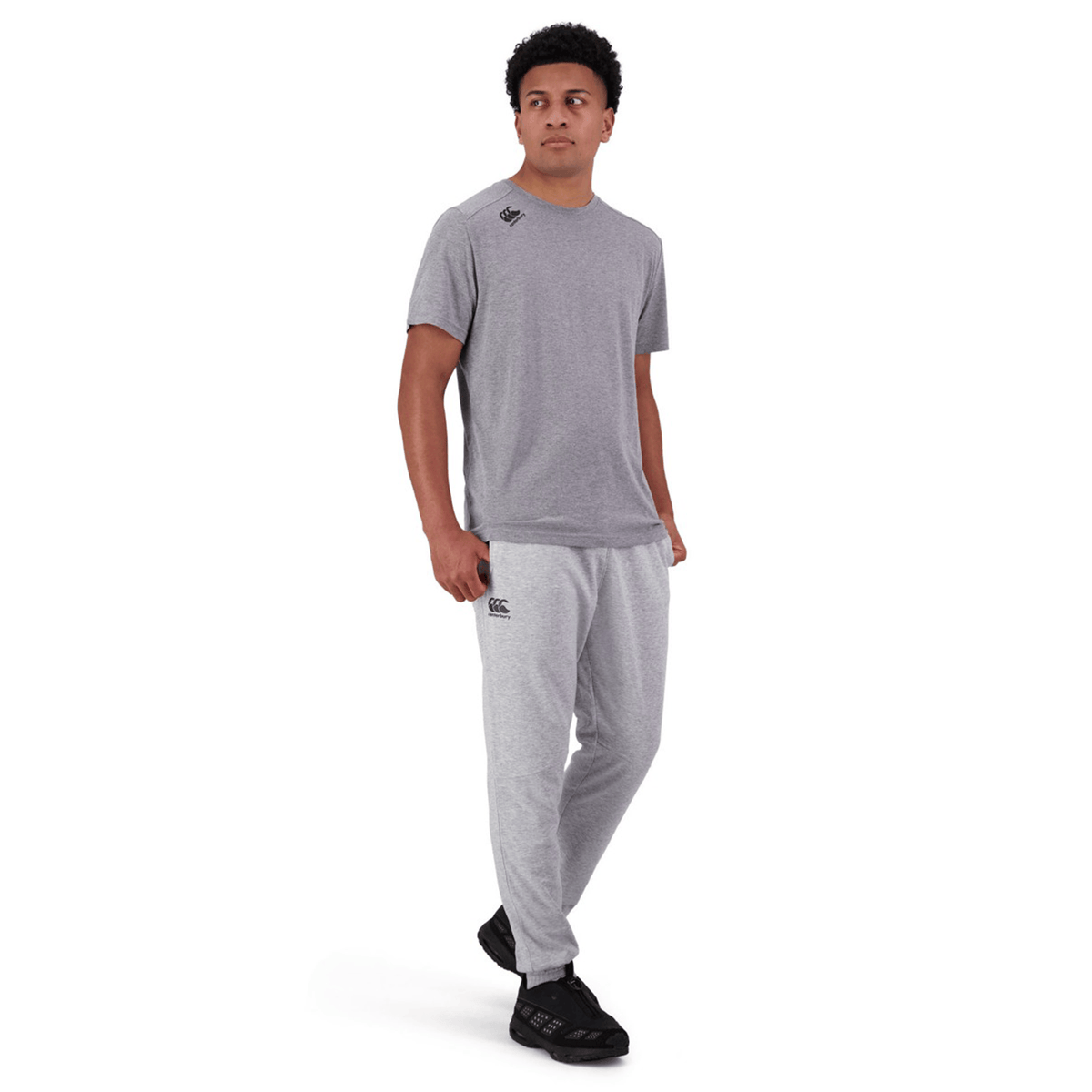 A person in a gray t-shirt and Canterbury Tempo Vapodri Hybrid Cuffed Pant with a tapered leg and elasticated waistband stands facing the camera with a neutral expression.