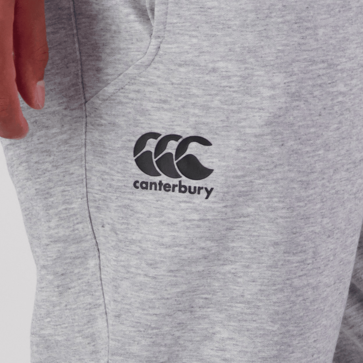Close-up of a person in gray Canterbury Tempo Vapodri Hybrid Cuffed Pant featuring the "Canterbury" logo. The tapered leg and elasticated waistband provide both style and comfort, with only part of the hand and pants visible.