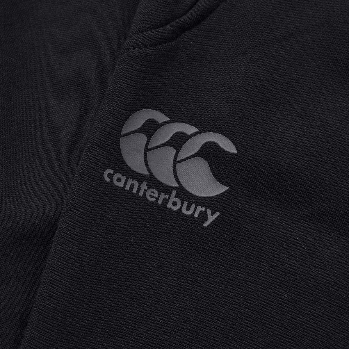 Close-up of a black Canterbury Tempo Vapodri Hybrid Cuffed Pant with the Canterbury logo of three grey overlapping shapes, featuring a tapered leg and elasticated waistband for comfort and style.