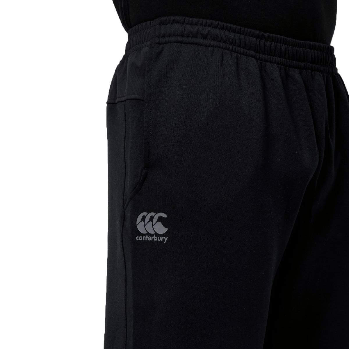 Close-up of the Canterbury Tempo Vapodri Hybrid Cuffed Pant in black showcases its tapered legs and elastic waistband. The side displays the Canterbury logo, enhancing the sleek design with authenticity.