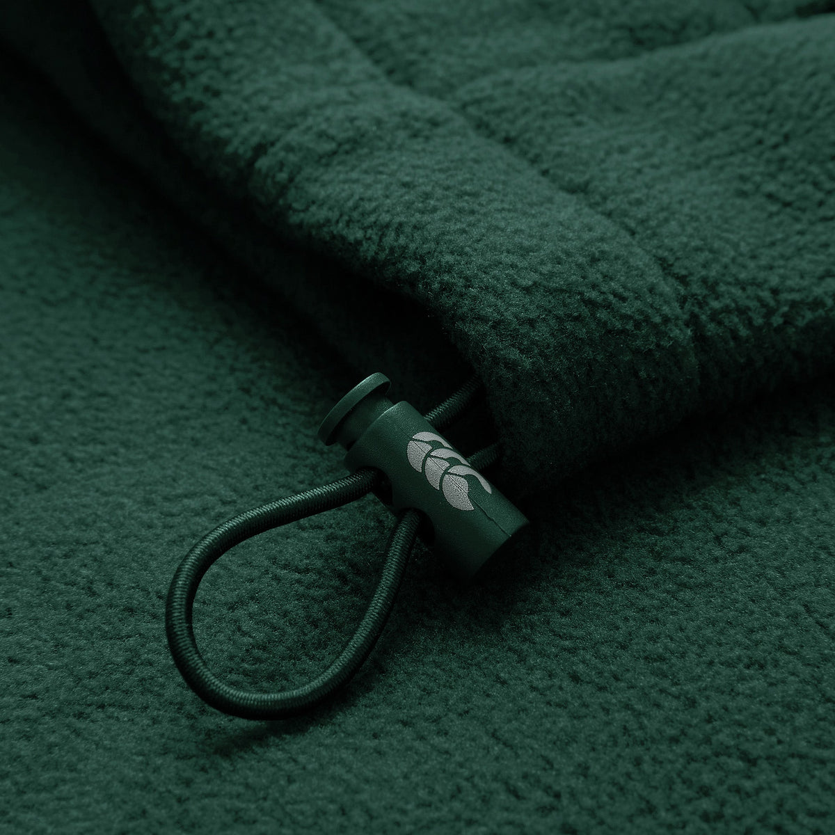 Close-up of the Ireland 26 Retro Fleece 1/4 Zip by Canterbury, showcasing its dark green fleece fabric, cord with a plastic toggle adorned with a small white leaf design—evoking the classic style of vintage Canterbury training pullovers.