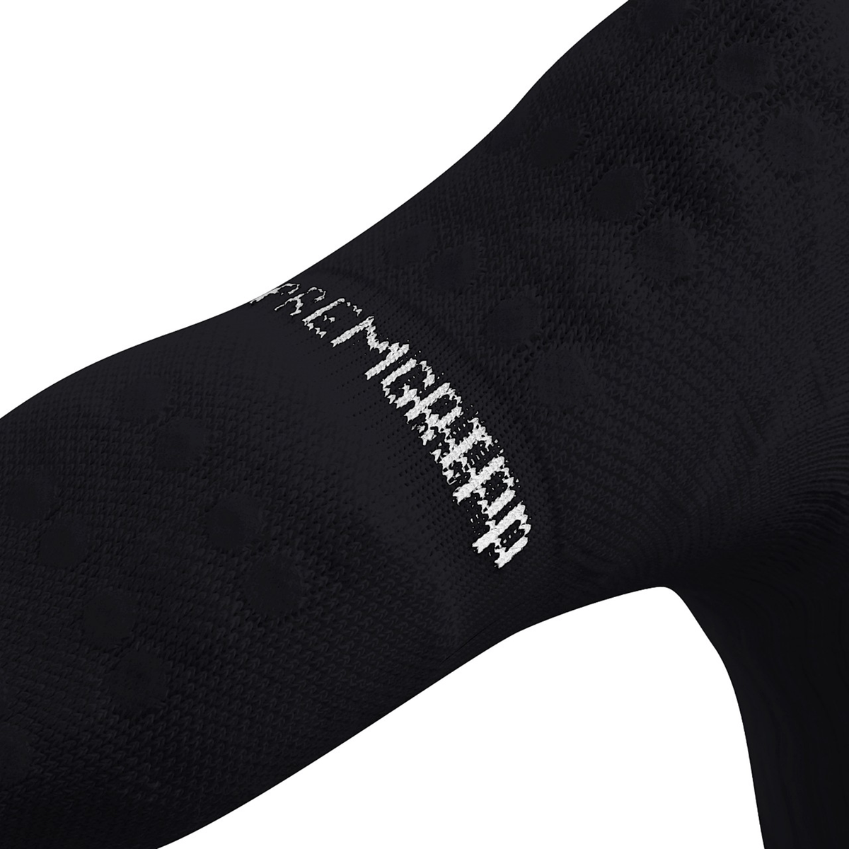 Close-up of a black fabric with white text reading "PAC MGMSRD." The texture, typical of a Canterbury Mid Calf Grip Sock by Canterbury, is visible with small dot patterns.