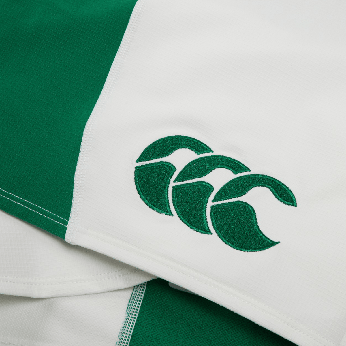 Close-up of the Ireland 24 Home Match Short by Canterbury, a white and green sports jersey, featuring a stitched emblem of three interlocking shapes on the green section, showcasing its durable design.