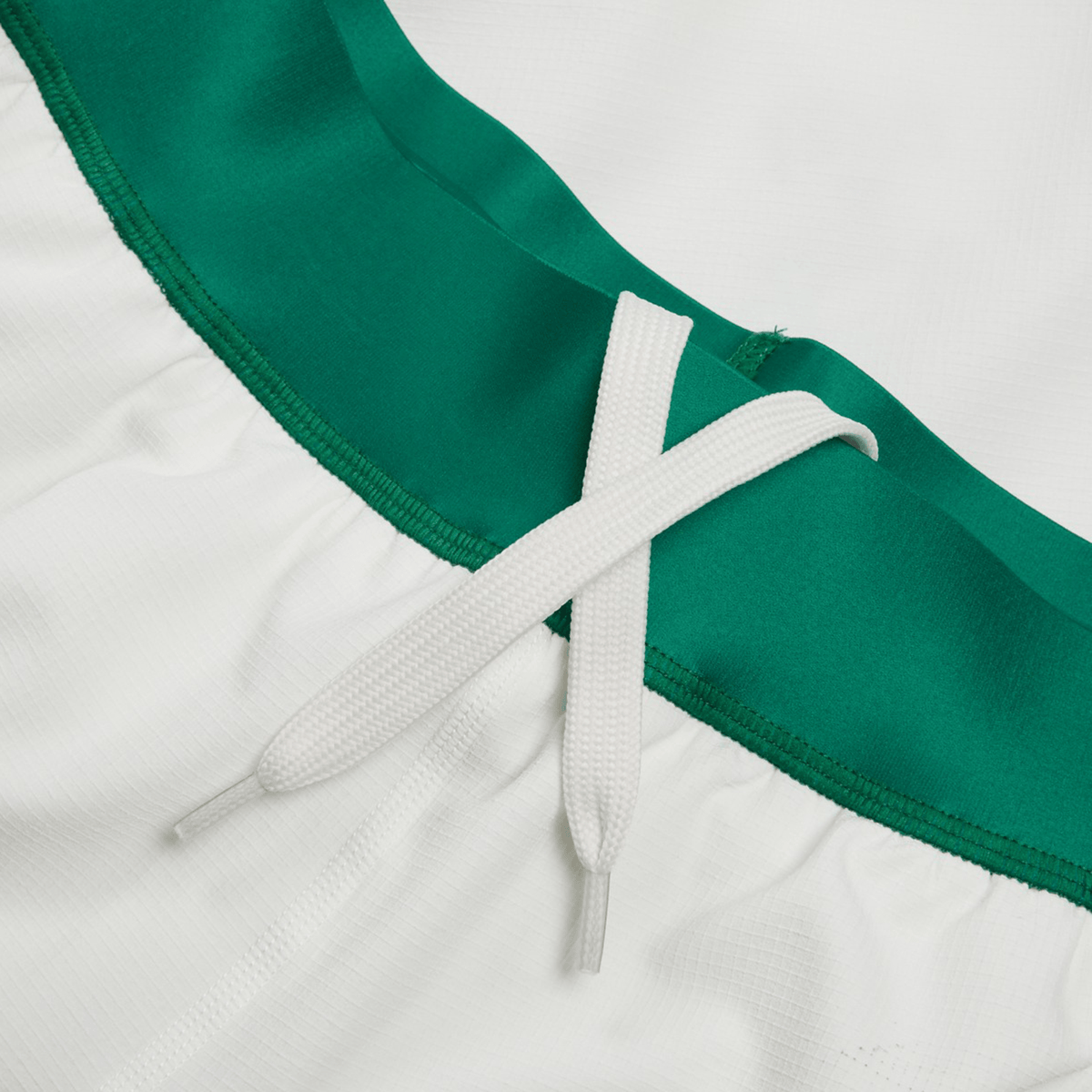 Close-up of the Ireland 24 Home Match Short by Canterbury, featuring a white garment with a green waistband and a white drawstring tie-up, crafted from moisture-wicking fabric.
