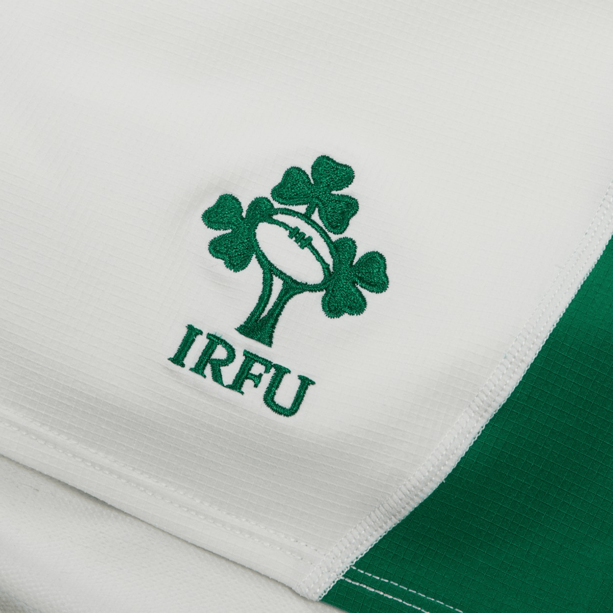 Close-up of the Irish Rugby Football Union (IRFU) logo, featuring a rugby ball with clover leaves, embroidered on moisture-wicking fabric. The Ireland 24 Home Match Short by Canterbury showcases this durable design on its white and green fabric.