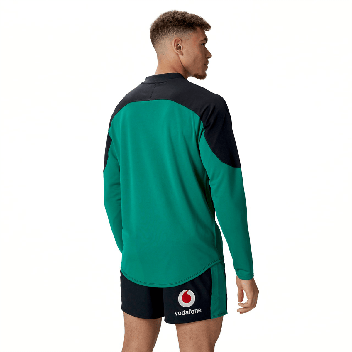 A person shown from the back is wearing the Ireland 25/26 Tech Drill Top by Canterbury, a green and black long-sleeve rugby top, paired with black Vodafone-logo shorts.