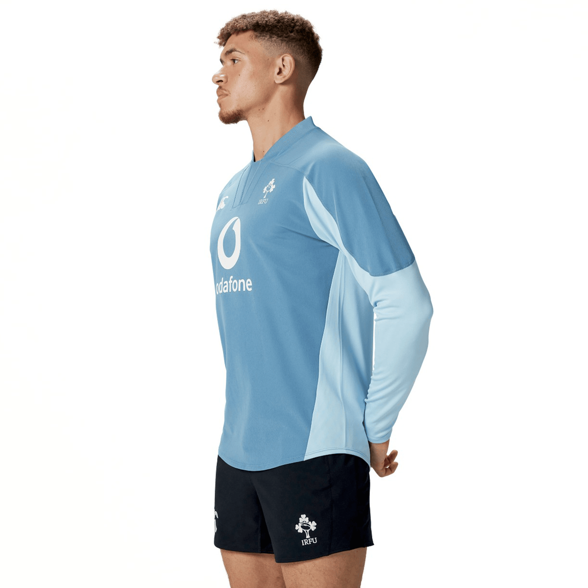 A man in profile wears the Ireland 25/26 Tech Drill Top by Canterbury with sponsor and logo, paired with navy shorts, against a plain white background.