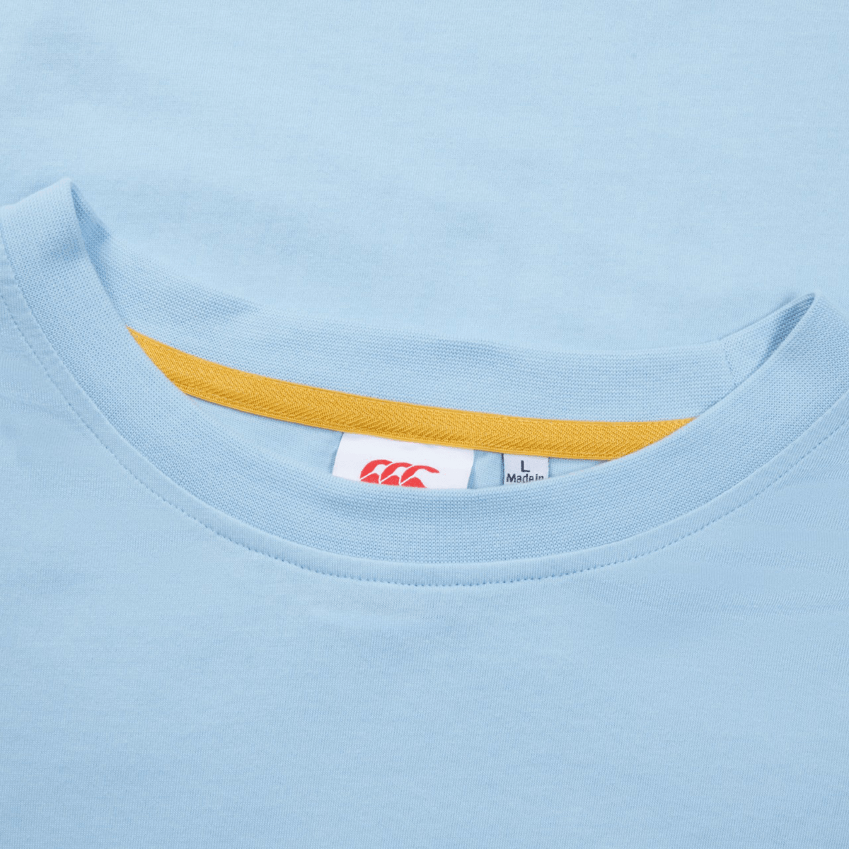 Close-up of a light blue Canterbury Uglies T-Shirt collar with a visible fabric tag inside showing sizing information and a small part of a yellow inner seam.