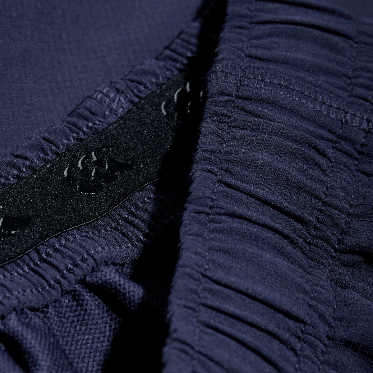 Close-up of dark blue fabric resembling Canterbury Yokohama shorts, showcasing textured patterns and ruching detail, highlighted by black elastic with stitched floral motifs. From the Bundle Canterbury 3-Pack Bundle collection.