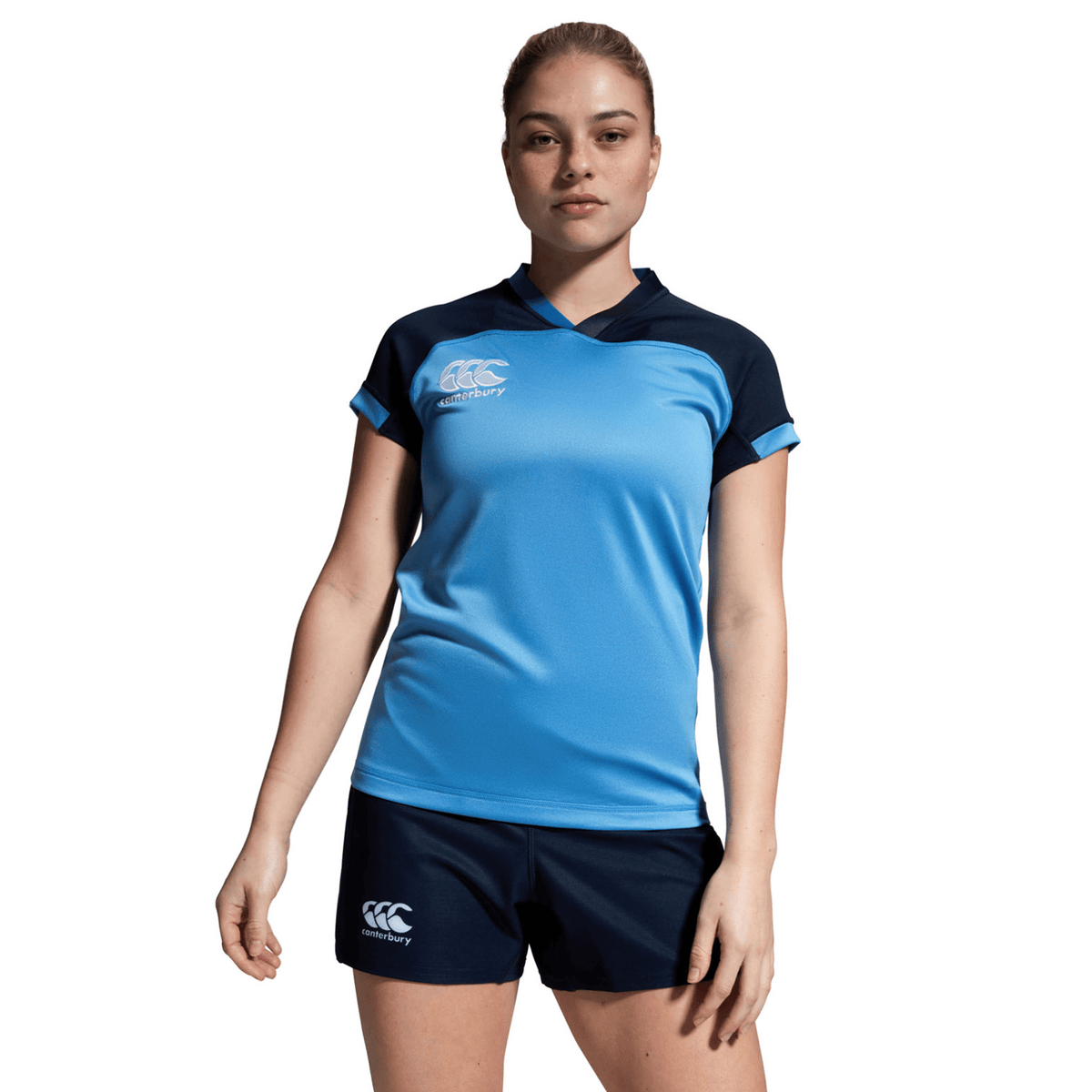 A person poses against a plain white background, wearing a blue sports jersey and navy Women&#39;s Canterbury Yokohama Shorts, both displaying the Canterbury logo. The Vapodri fabric offers advanced comfort.