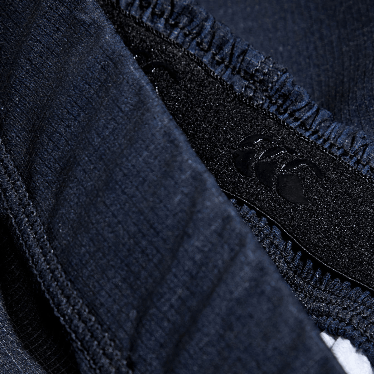 Close-up of the navy woven texture fabric and stitched seam of the Women&#39;s Canterbury Yokohama Short 3-Pack Bundle by Bundle Canterbury, showcasing a small black logo on a tag. This durable material is ideal for providing strength and reliability during women&#39;s intense rugby matches.