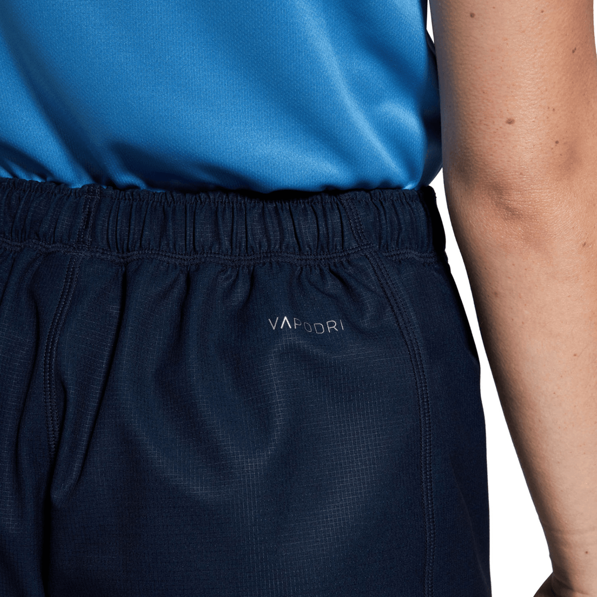A person is seen from the back wearing the Women&#39;s Canterbury Yokohama Short, featuring dark athletic shorts and a blue shirt with &quot;VaporDri&quot; branding and the Canterbury logo.