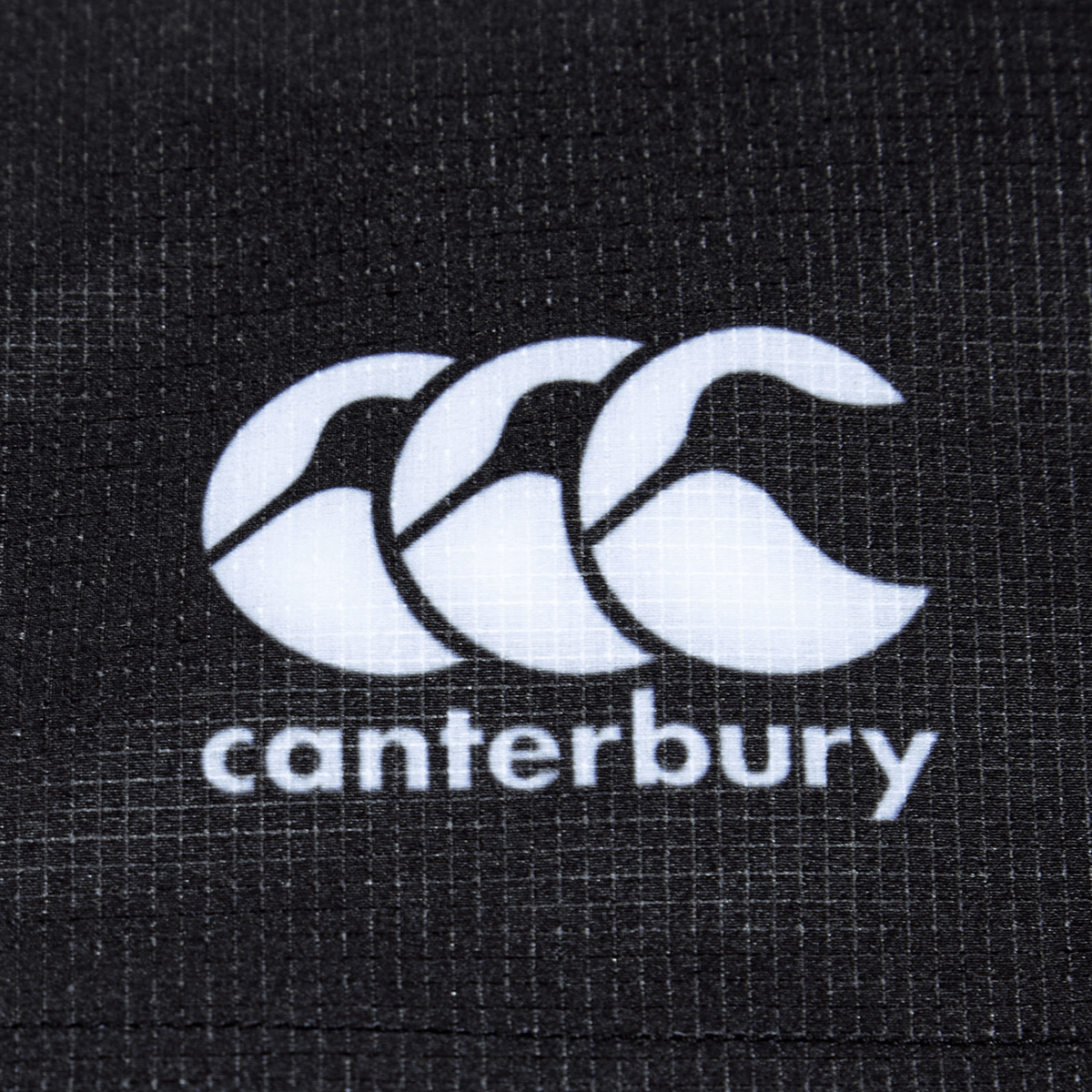 Close-up of the Bundle Canterbury logo on a textured black fabric background, showcasing the durable fabric of the Women&#39;s Canterbury Yokohama Short 3-Pack Bundle.