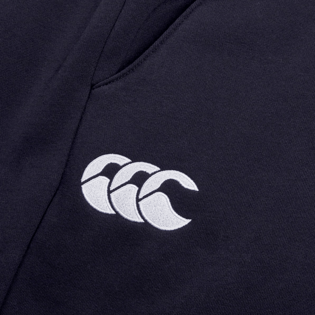 Close-up of a dark fabric with a white Canterbury logo featuring three overlapping curved shapes, crafted from cotton blend fleece on Women&#39;s Leisure Sweatpants by Canterbury.