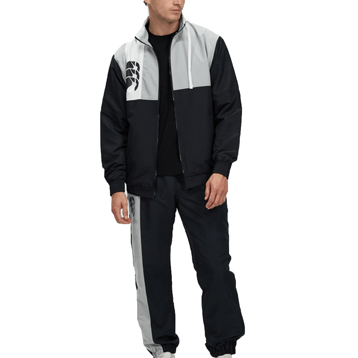 Man wearing a black and gray Canterbury Legends Woven Track Jacket with a distinctive logo on the jacket, standing against a white background.