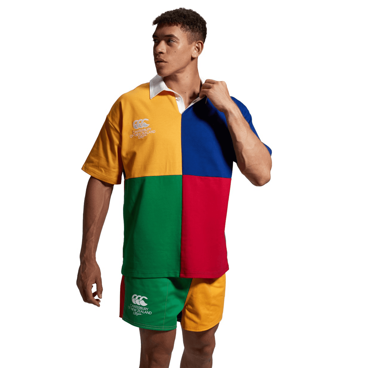 A person wearing a vibrant Canterbury Harlequin Rugby Jersey, divided into four quadrants of yellow, green, blue, and red with logos on the chest and left leg, stands against a white background.