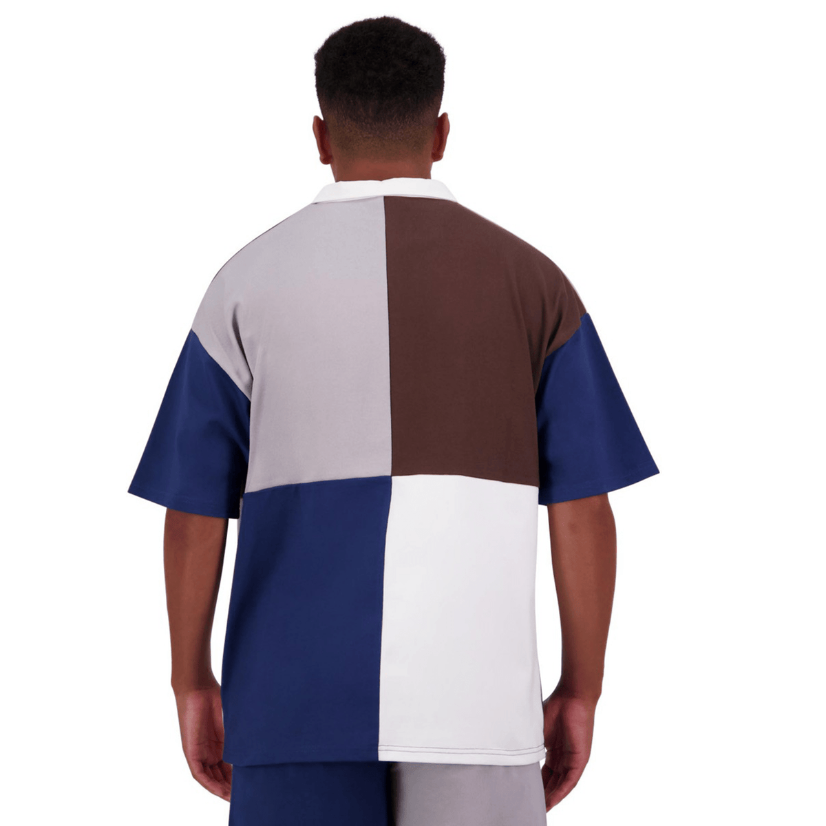 A person wearing a short-sleeved Canterbury Harlequin Block S/S Rugger shirt, featuring white, blue, brown, and gray quadrants, viewed from the back.