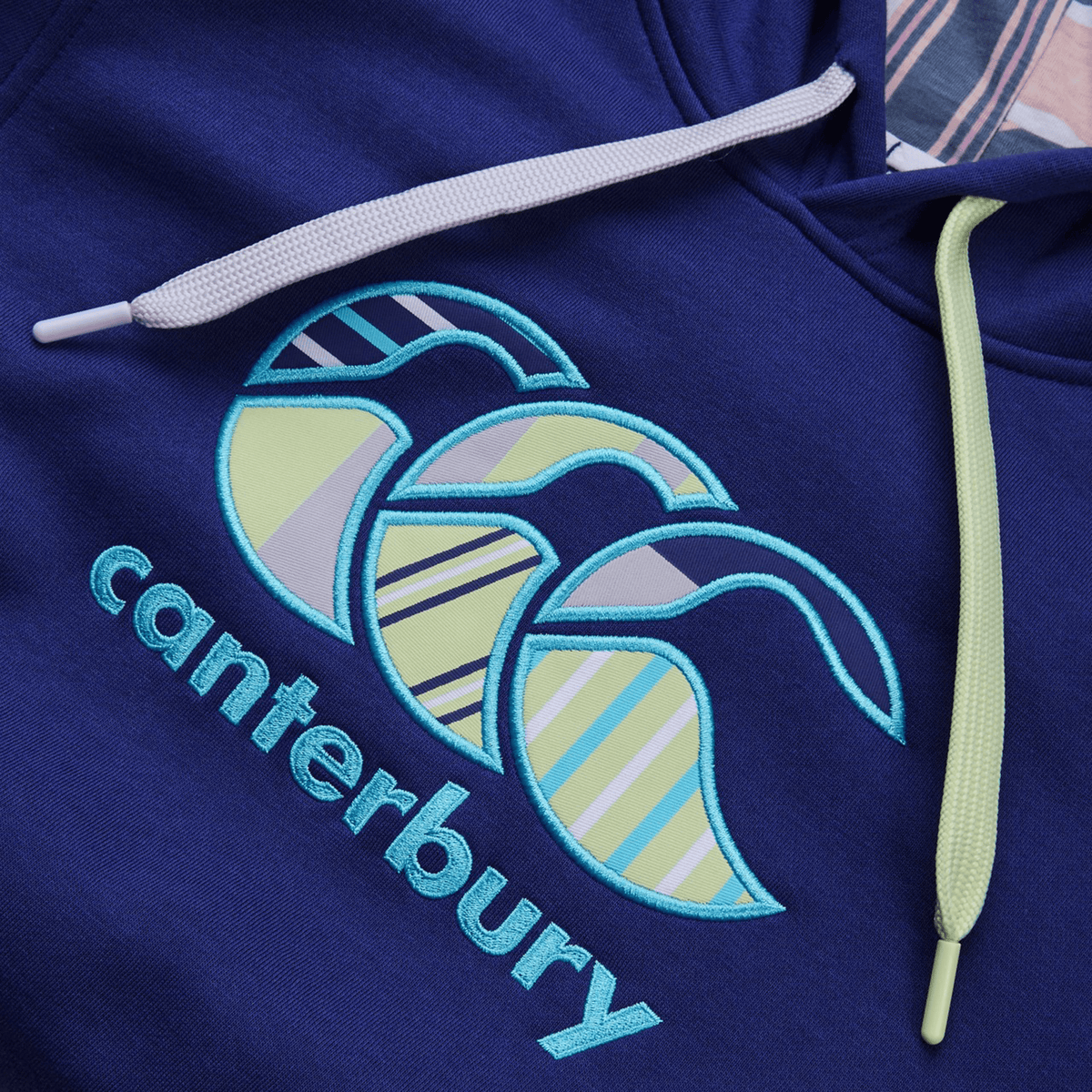 The Canterbury Women&#39;s Uglies Hoodie features &quot;Canterbury&quot; in blue with vibrant yellow and blue abstract shapes and striped patterns. Light-colored drawstrings elegantly hang above the logo, enhancing its stylish appeal.