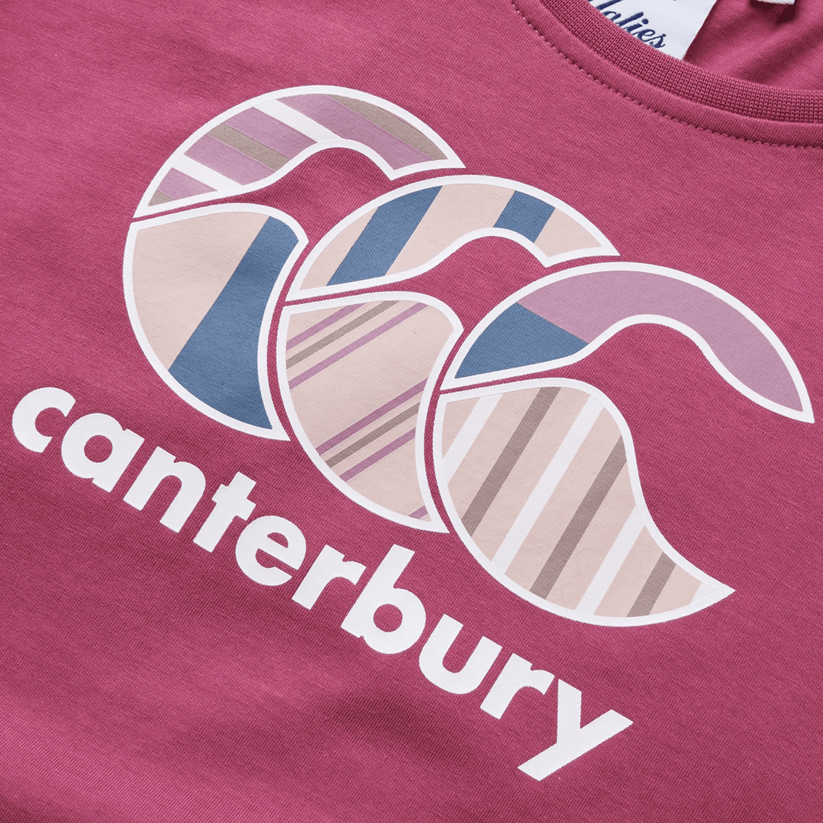 Close-up of a maroon Women&#39;s Canterbury Uglies T-Shirt, highlighting the brand name &quot;Canterbury&quot; and a unique heat-pressed logo featuring overlapping crescent shapes in solid bold colors and varied patterns.