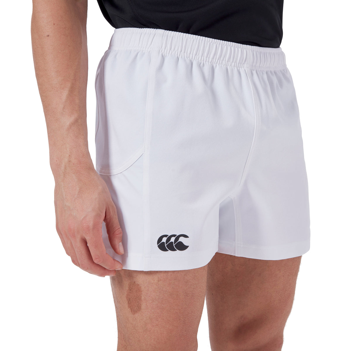 A person is wearing the white Canterbury Advantage Short 2.0, which features a black logo on the left leg, paired with a dark shirt. These shorts, equipped with an elastic waistband and side pockets, emphasize performance sustainability due to their recycled content.