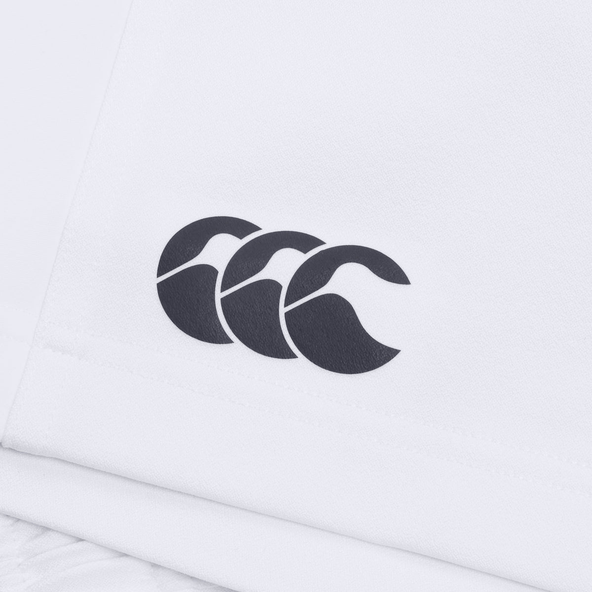 Close-up of the Canterbury Advantage Short 2.0, a white garment featuring a black logo with three stylized shapes resembling waves or arches, made by Canterbury with recycled content.