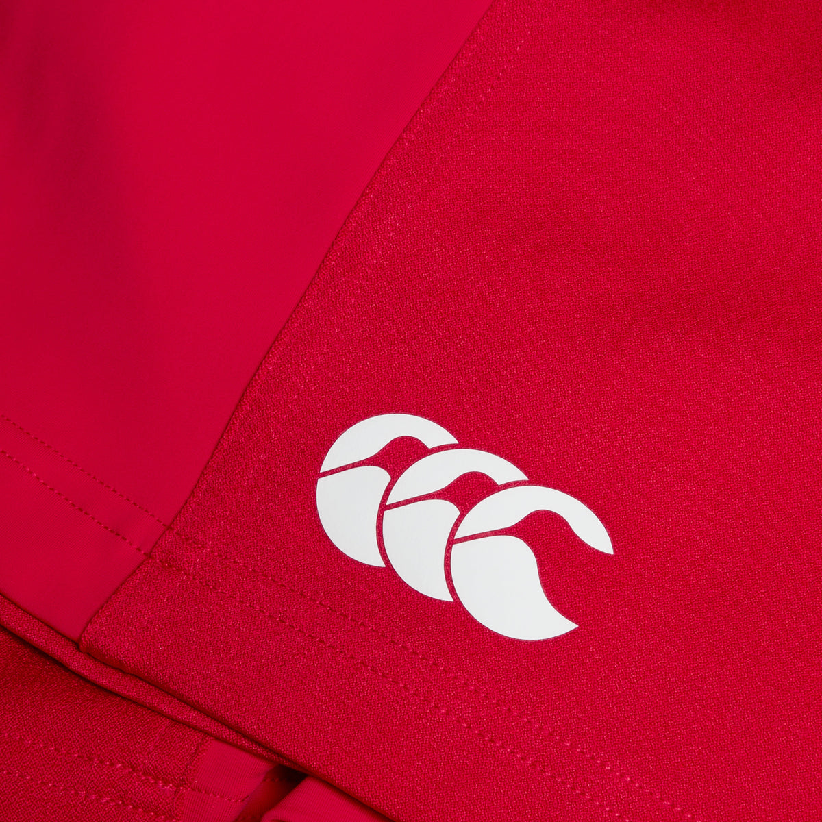 A close-up of a red fabric featuring the white logo of Canterbury Advantage Short 2.0, consisting of three overlapping curved shapes made with recycled content.