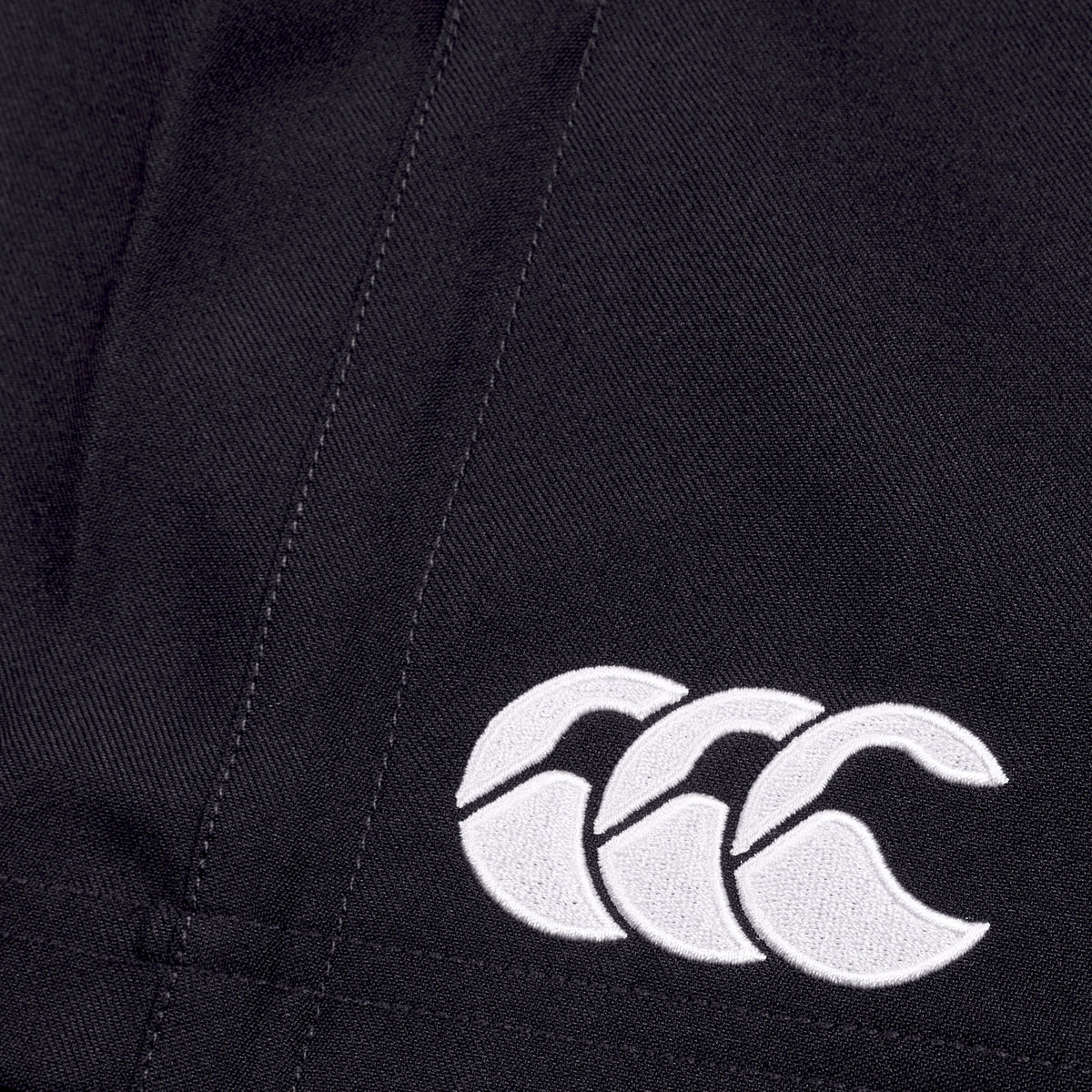 Close-up of a Canterbury Player's Drill Short in black, featuring a white embroidered logo of three interlocking crescent shapes, crafted from recycled fabric for sustainable athletic performance.