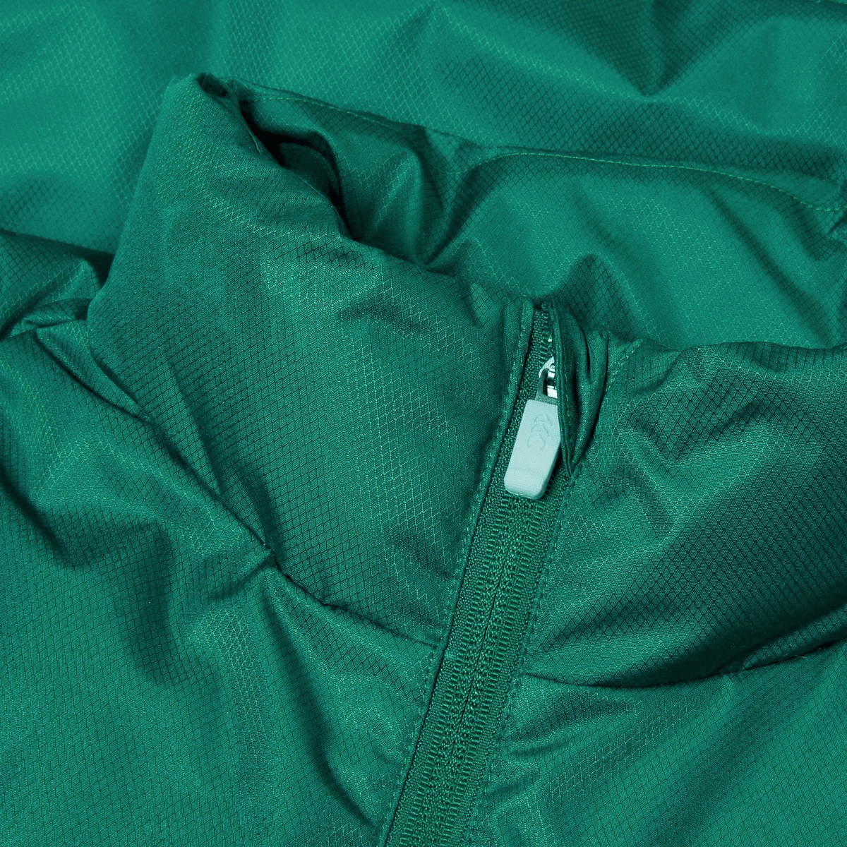 Close-up of a teal-colored Ireland 24 Puffer Jacket by Canterbury, featuring textured fabric and a visible front zipper. Just In at Canterbury.