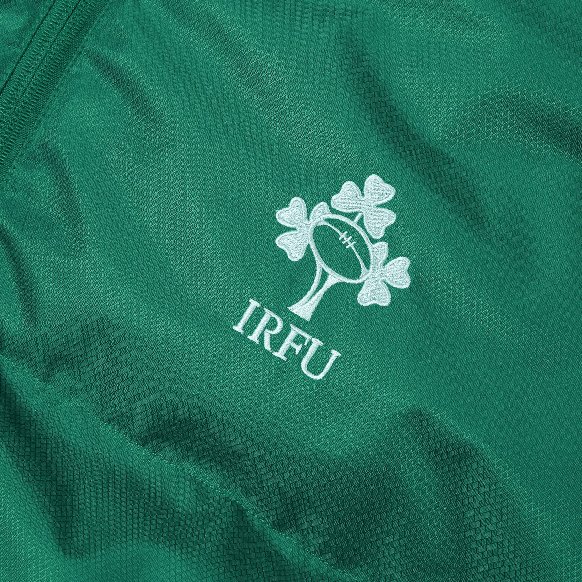 Close-up of green fabric showcasing the Irish Rugby Football Union logo, featuring a rugby ball and three shamrocks. You can find this detailed emblem on the latest Ireland 24 Puffer Jacket by Canterbury.