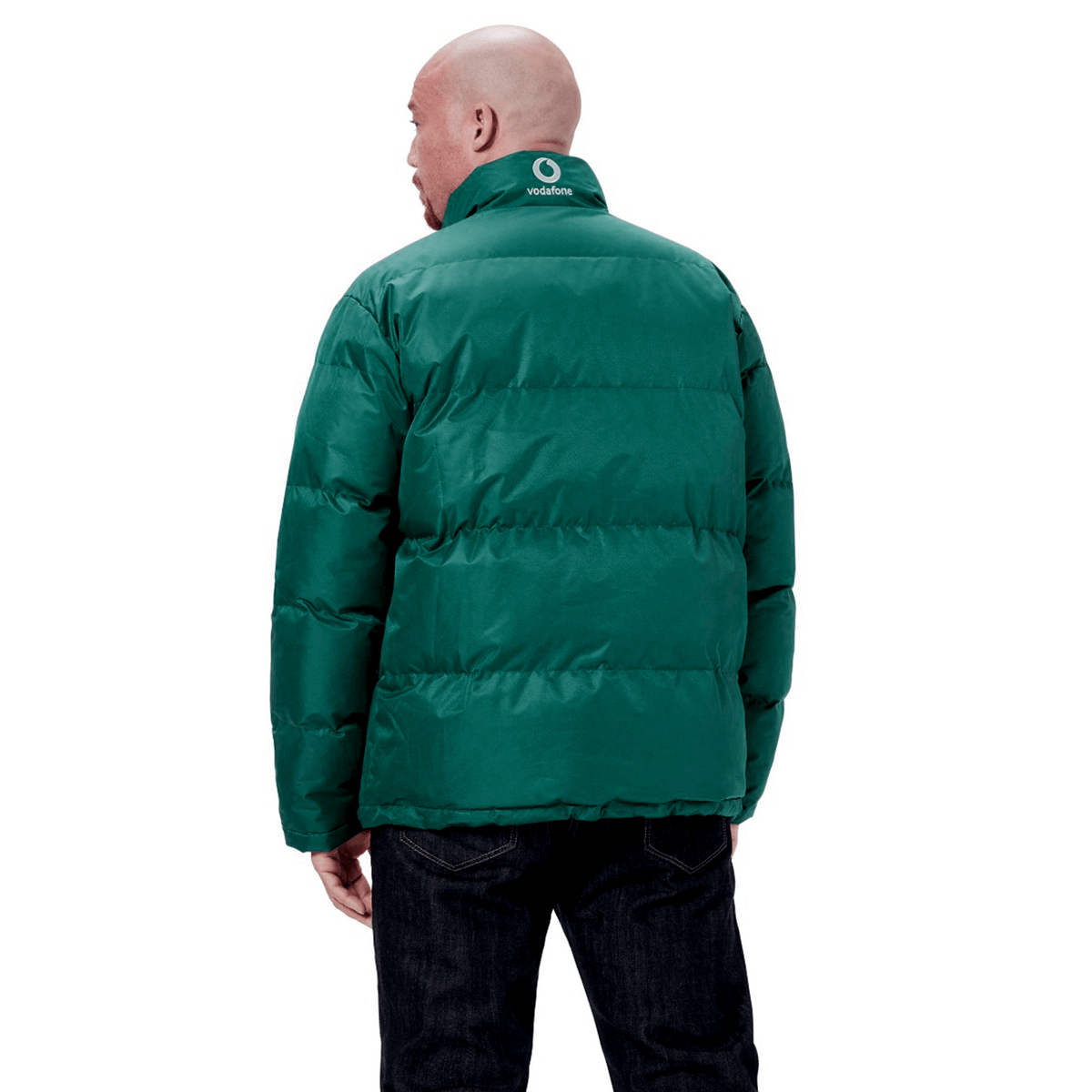 A bald person wearing the green Ireland 24 Puffer Jacket by Canterbury, featuring white Canterbury branding on the collar, is seen from the back. The jacket is paired with dark jeans.