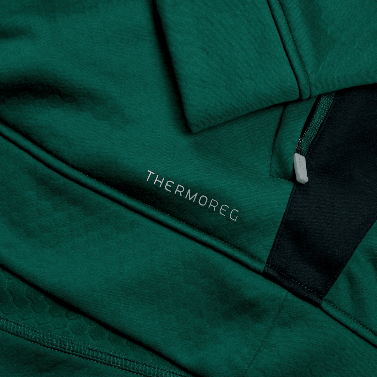 Close-up of the Ireland 1/4 Zip Training Top 25/26 by Canterbury, showing its green textured fabric, &quot;THERMOREG&quot; in white, and the signature black Canterbury 1/4 zip panel.