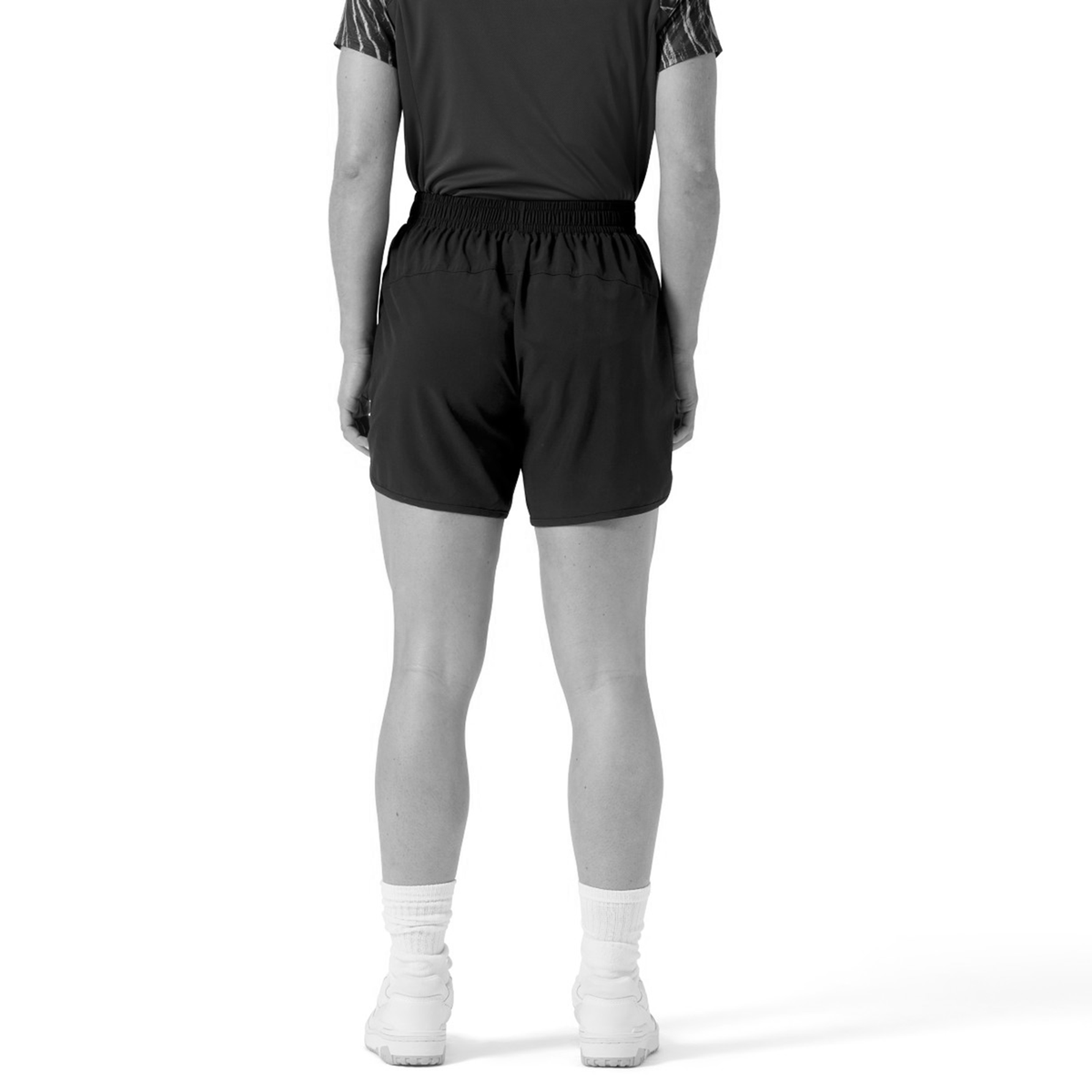 A person faces away from the camera, wearing a short-sleeve shirt, socks, sneakers, and Canterbury Women&#39;s Ireland 25/26 Woven Gym Short, with a plain white background.