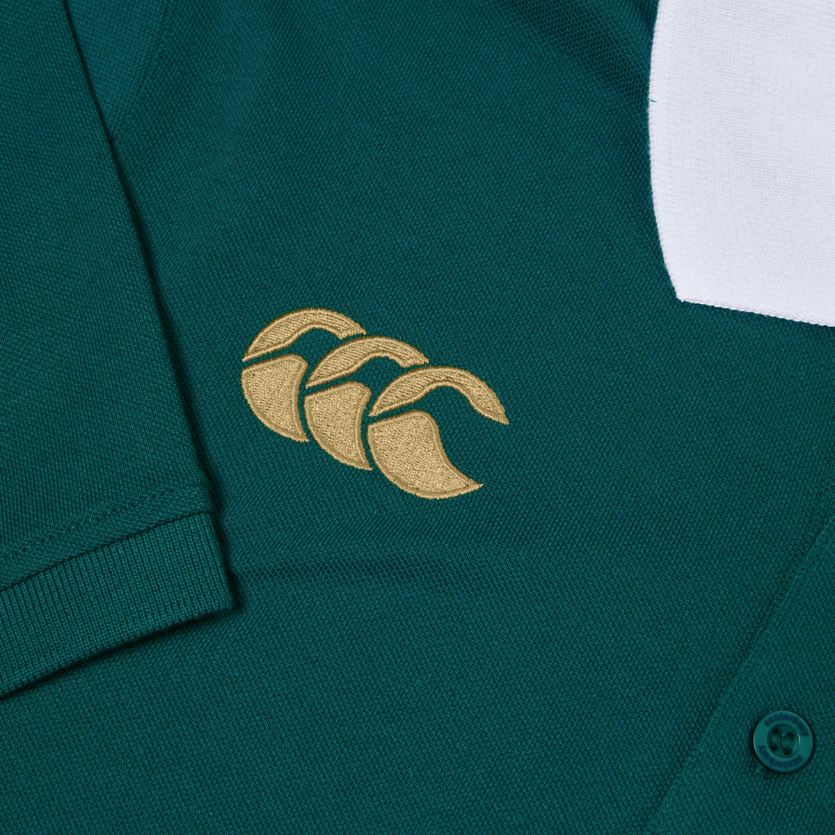 Close-up of the Ireland 150th Anniversary Polo by Canterbury, ideal for rugby enthusiasts, showcasing a gold three-leaf clover logo and a white section at the top right. Celebrate IRFU 150 Years with this iconic piece from Canterbury.