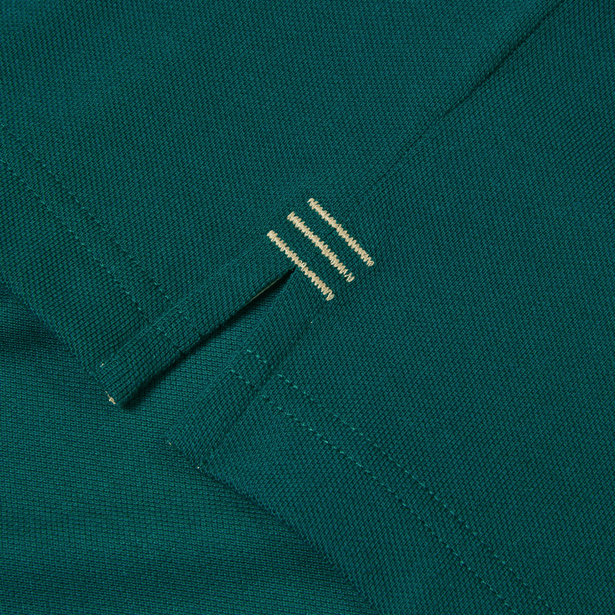 Close-up of a green fabric from the Canterbury Ireland 150th Anniversary Polo, showcasing a small embroidered detail with three horizontal beige stitches—ideal for rugby fans celebrating 150 years of IRFU history.