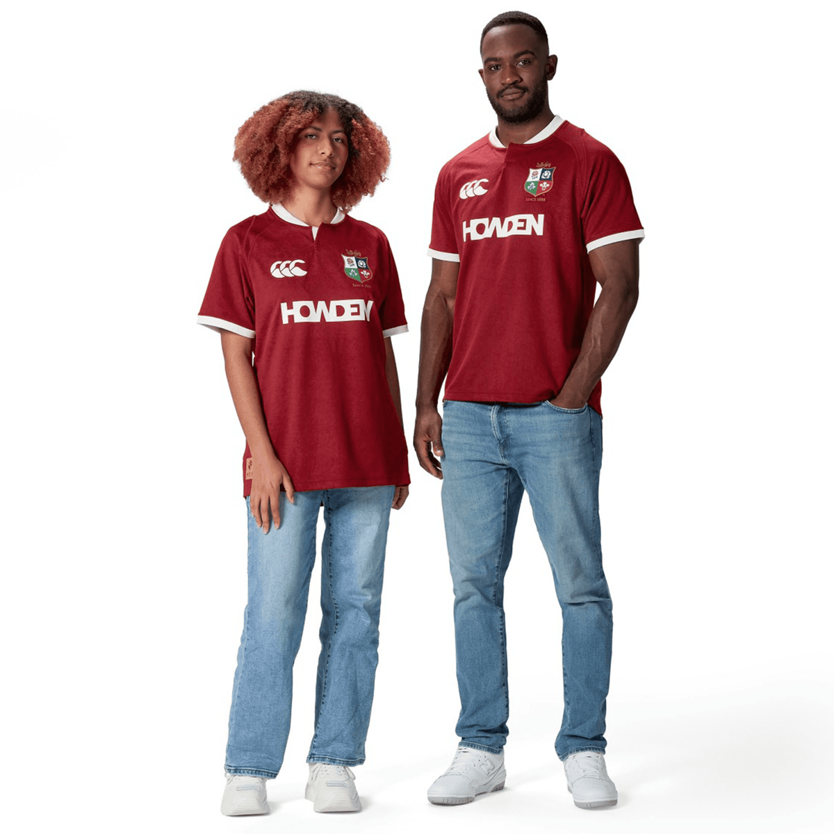 Two people wearing matching red *British &amp; Irish Lions 2025 Players Jerseys by Canterbury* and jeans, standing against a white background. The moisture-wicking fabric of their Canterbury attire keeps them comfortable and stylish.