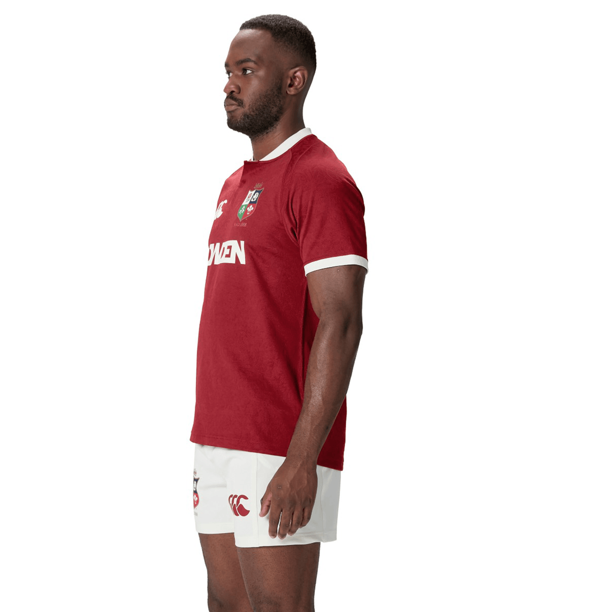 Wearing a maroon British &amp; Irish Lions 2025 Players Jersey by Canterbury and white shorts, a person stands in profile against a white background, highlighting the garment's moisture-wicking fabric.