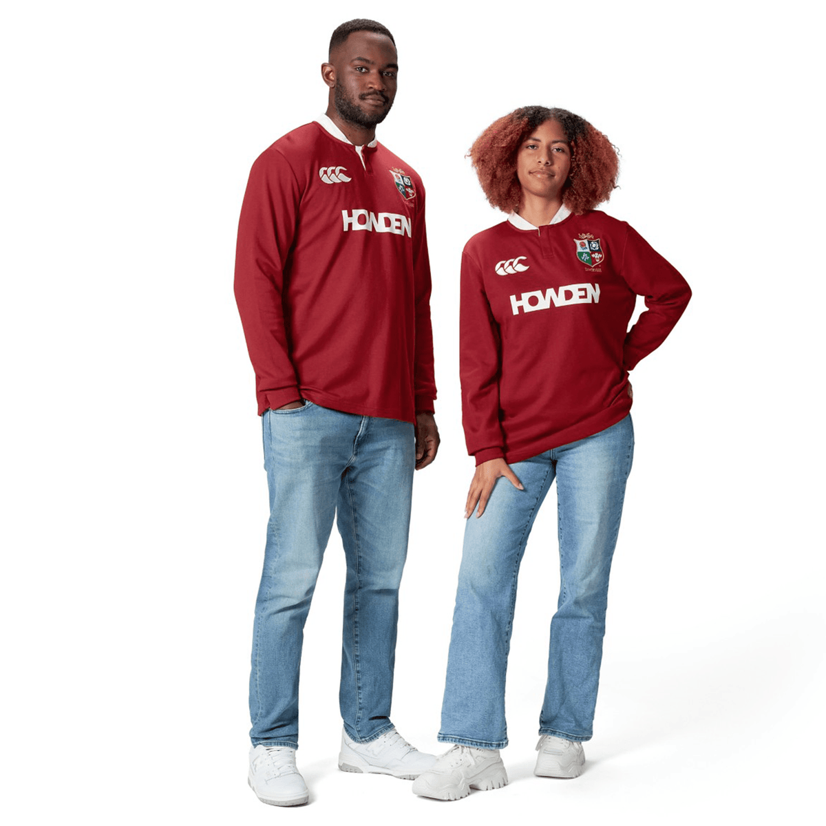 Two individuals dressed in maroon sports jerseys featuring the "British &amp; Irish Lions 2025" design by Canterbury, made from moisture-wicking fabric for superior comfort, are complemented by blue jeans and white shoes as they stand against a white backdrop.