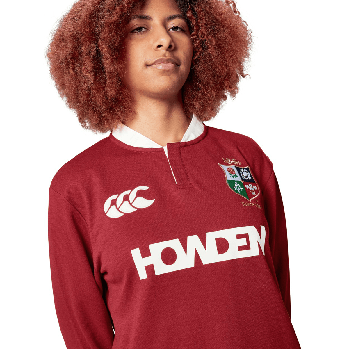 The individual is wearing the British &amp; Irish Lions 2025 Long Sleeve Classic Jersey by Canterbury, which features a maroon color with logos and "Howden" emblazoned on the front. It boasts a crisp white collar, giving it a classic appearance. The long sleeves are made from moisture-wicking fabric to provide comfort during intense matches.