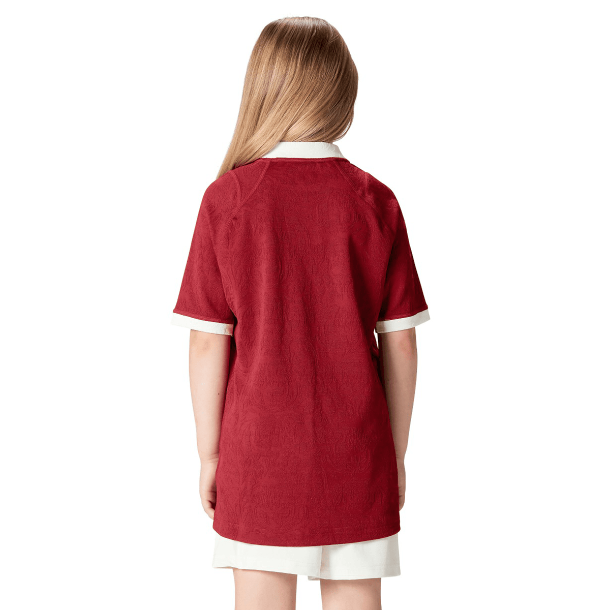 A child with long hair, facing away, sports the Youth British &amp; Irish Lions 2025 Players Jersey by Canterbury, featuring a red design and subtle ergonomic paneling.