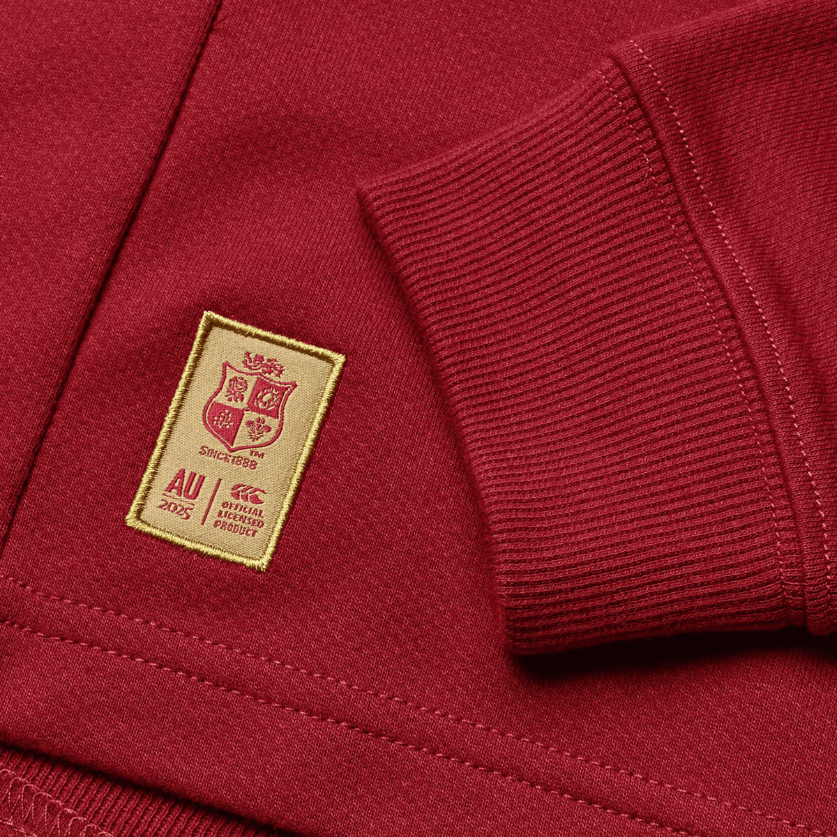 The Youth British &amp; Irish Lions 2025 Long Sleeve Classic Jersey by Canterbury is maroon with a sewn beige patch featuring shields and text &quot;Since 1829&quot; and &quot;AU 2025.&quot; Made from moisture-wicking fabric, it&#39;s ideal for active wearers.